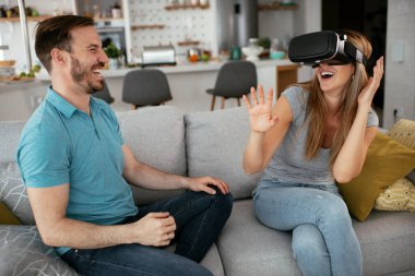 Mutlu çift oturma odasında sanal gerçeklik gözlükleriyle eğleniyor. Evde video oyunu oynayan ve eğlenen genç bir çift..