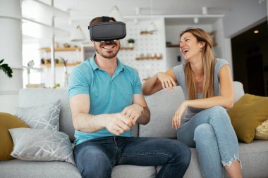 Mutlu çift oturma odasında sanal gerçeklik gözlükleriyle eğleniyor. Evde video oyunu oynayan ve eğlenen genç çift..