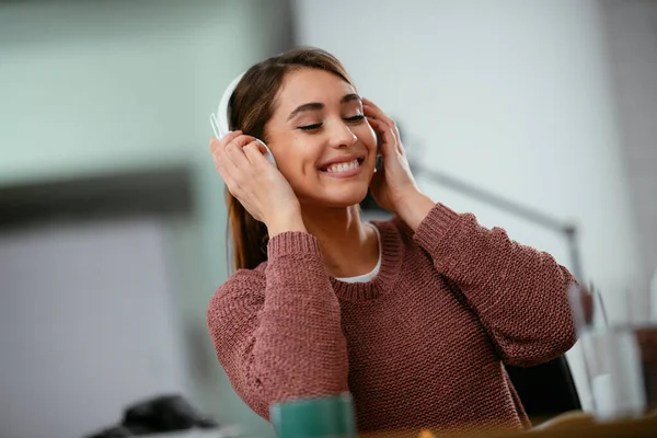 Young woman in office with headphones. Young casual businesswoman enjoying in her favorite song over headphones and singing while working on laptop in the office.