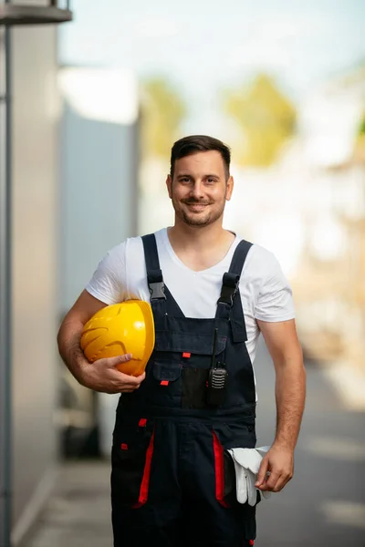 Portrait of smiling worker holding yellow helmet in hand