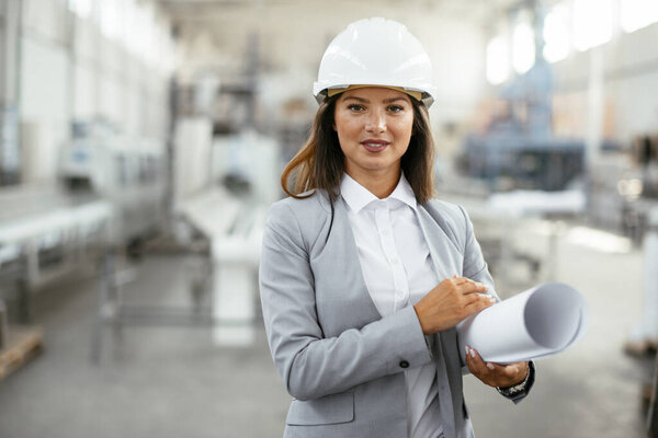 portrait of beautiful architect woman with blueprint standing in a factory