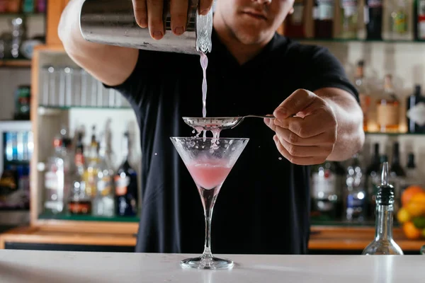 Expert barman making cocktail at night club. Bartender preparing red cocktail at the bar.