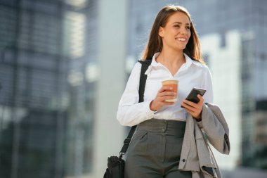 Ofis binasının yanında yürürken elinde cep telefonuyla işe giden güzel bir kadın..