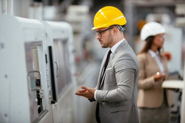 Fabrikadaki iş adamı ve iş kadını. Fabrika üretim hattında kalite kontrolde çalışan iki profesyonel insan..