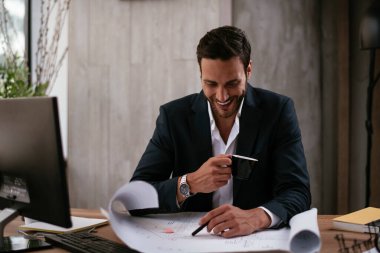 Genç iş adamı projeler üzerinde çalışıyor. Ofiste çalışan takım elbiseli yakışıklı bir iş adamı..