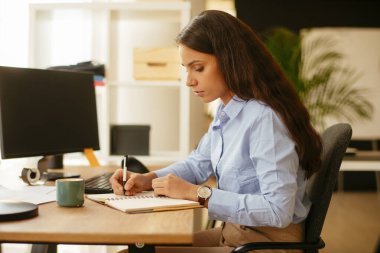 Güzel iş kadını ofisinde oturuyor ve işyerinde çalışıyor. 