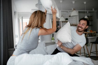 Genç çift yatakta yastık kavgası yapıyor. Mutlu çift evde eğleniyor.