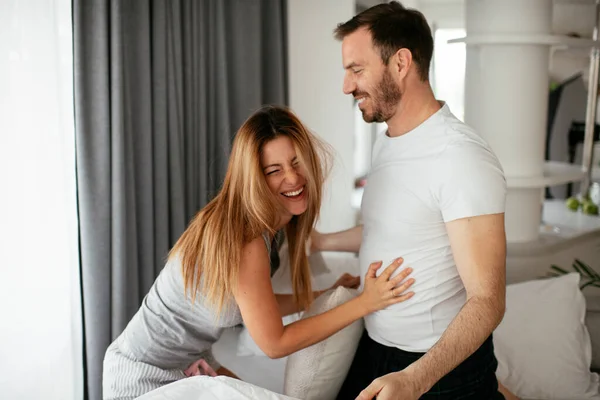 Young couple fighting pillows on the bed. Happy couple having fun at home