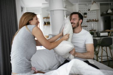 Genç çift yatakta yastık kavgası yapıyor. Mutlu çift evde eğleniyor.