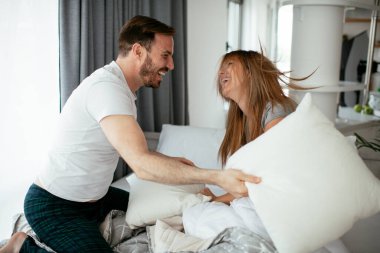 Genç çift yatakta yastık kavgası yapıyor. Mutlu çift evde eğleniyor.