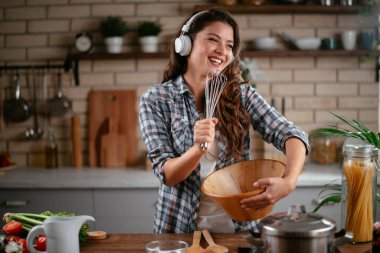 Sevimli, sevimli, neşeli, güzel, modaya uygun, modaya uygun, mutfakta müzik dinleyen kız. Mutfakta şarkı söyleyen genç mutlu kadın.