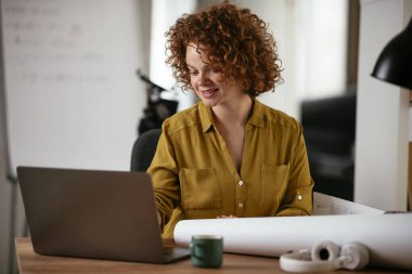 Güzel bir iş kadını proje üzerinde çalışıyor. Ofiste kıvırcık saçlı genç bir kadın var..