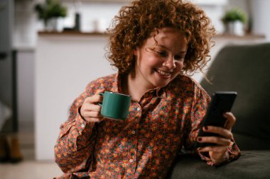 Telefonu kullanan genç bir kadın. Güzel kadın evde eğleniyor..