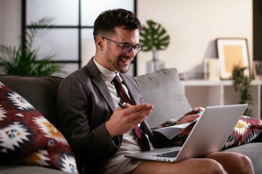 Evde pantolonsuz çalışan bir iş adamı. Genç adam video görüşmesi sırasında bilgisayarı kullanıyor..