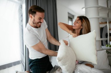 Genç çift yatakta yastık kavgası yapıyor. Mutlu çift evde eğleniyor.