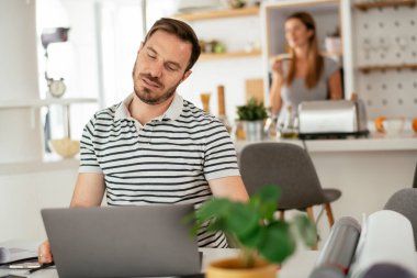 Evde çalışan yorgun bir adam. Genç adam dizüstü bilgisayar kullanıyor.