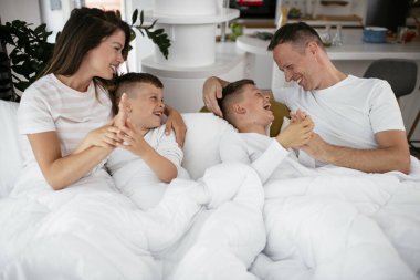 Genç bir aile yatakta eğleniyor. Oğulları yatakta dinlenen mutlu ebeveynler..