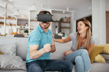 Mutlu çift oturma odasında sanal gerçeklik gözlükleriyle eğleniyor. Evde video oyunu oynayan ve eğlenen genç çift..