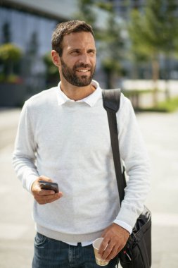 Yakışıklı genç işadamı telefon kullanıyor ve sokakta kahve içiyor.
