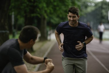 Gençler yarış pistinde antrenman yapıyor. İki genç arkadaş atletizm pistinde koşuyor.