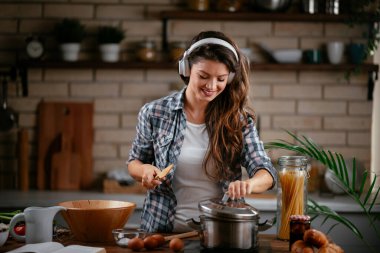Sevimli, sevimli, neşeli, güzel, modaya uygun, modaya uygun, mutfakta müzik dinleyen kız. Mutfakta şarkı söyleyen genç mutlu kadın.
