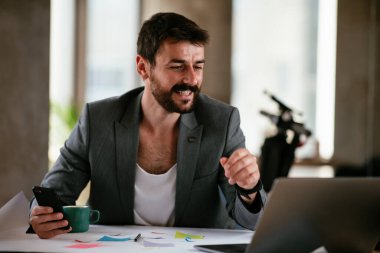 İş adamı proje üzerinde çalışıyor. Ofiste akıllı telefon kullanan genç bir işadamı..