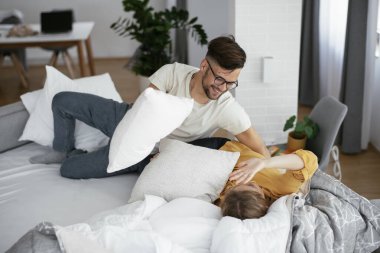 Erkek arkadaş ve kız arkadaş yatakta yastık kavgası yapıyor. Mutlu çift evde eğleniyor.