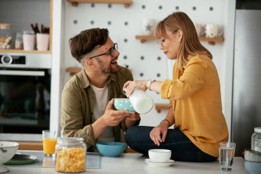 Genç çift evde kahvaltı hazırlıyor. Sevgi dolu çift mutfakta mısır gevreği yiyor..