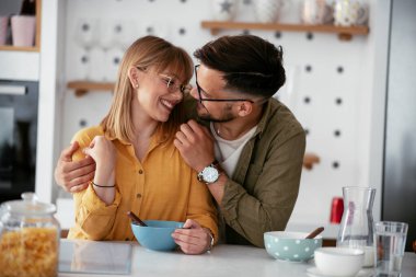 Genç çift evde kahvaltı hazırlıyor. Sevgi dolu çift mutfakta mısır gevreği yiyor..