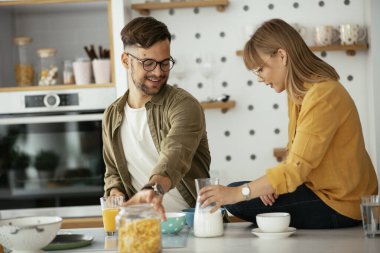 Genç çift evde kahvaltı hazırlıyor. Sevgi dolu çift mutfakta mısır gevreği yiyor..