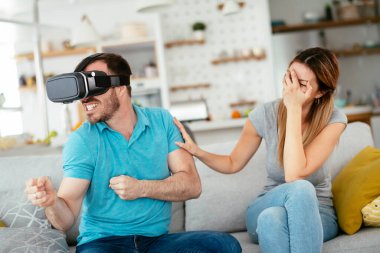 Mutlu çift oturma odasında sanal gerçeklik gözlükleriyle eğleniyor. Evde video oyunu oynayan ve eğlenen genç bir çift..