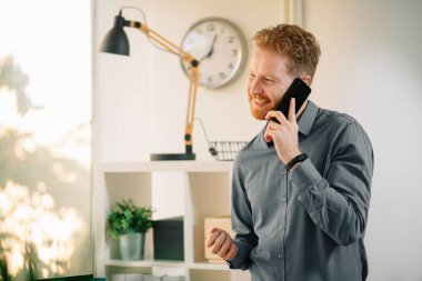 Ofiste akıllı telefon kullanan kızıl saçlı yakışıklı bir iş adamı.