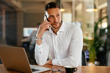 İş adamı telefonda iş konuşuyor. Genç işadamı ofiste telefonda konuşuyor..