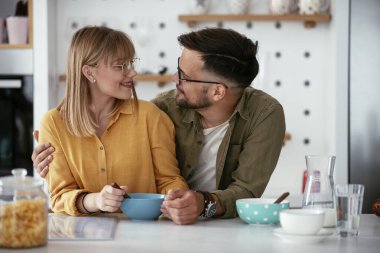 Genç çift evde kahvaltı hazırlıyor. Sevgi dolu çift mutfakta mısır gevreği yiyor..