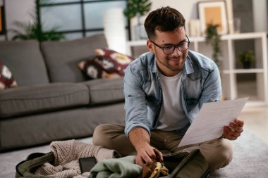 Giysilerini seyahat çantasına koyan gülümseyen genç adam. Yolculuğa hazırlanan adam.