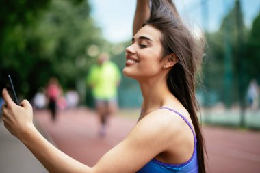 Egzersiz yapmaktan dinlenen güzel bir kadın. Genç sporcu kadın bankta oturuyor ve telefonu kullanıyor..