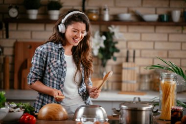 Sevimli, sevimli, neşeli, güzel, modaya uygun, modaya uygun, mutfakta müzik dinleyen kız. Mutfakta şarkı söyleyen genç mutlu kadın.