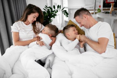 Genç bir aile yatakta eğleniyor. Oğulları yatakta dinlenen mutlu ebeveynler..