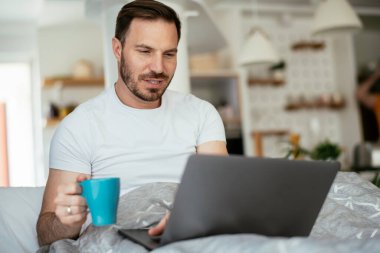 Genç adam yatakta film izliyor ve kahve içiyor. Yakışıklı adam sabahları eğleniyor..