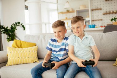 Küçük kardeşler oturma odasında video oyunu oynarken eğleniyorlar.