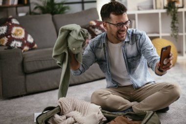 Giysilerini seyahat çantasına koyan gülümseyen genç adam. Yolculuğa hazırlanan adam.