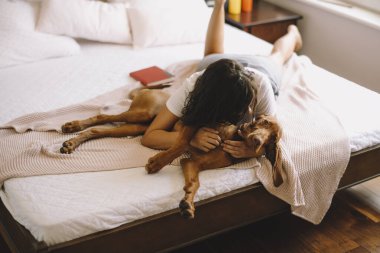 Güzel genç bir kadın köpeğiyle yatakta oynuyor.