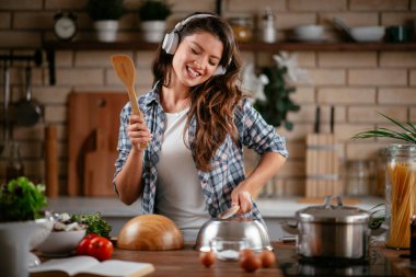 Sevimli, sevimli, neşeli, güzel, modaya uygun, modaya uygun, mutfakta müzik dinleyen kız. Mutfakta şarkı söyleyen genç mutlu kadın.