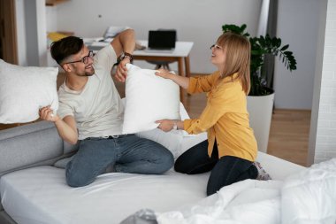 Erkek arkadaş ve kız arkadaş yatakta yastık kavgası yapıyor. Mutlu çift evde eğleniyor.