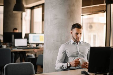 Beyaz gömlekli yakışıklı iş adamı ofiste bilgisayar kullanıyor.