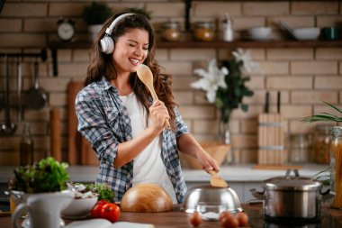 Sevimli, sevimli, neşeli, güzel, modaya uygun, modaya uygun, mutfakta müzik dinleyen kız. Mutfakta şarkı söyleyen genç mutlu kadın.