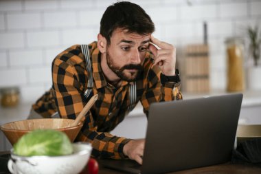 Mutfaktaki yakışıklı adamın portresi. Genç adam video ararken yemek pişiriyor..