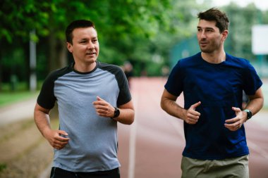Gençler yarış pistinde antrenman yapıyor. İki genç arkadaş atletizm pistinde koşuyor.