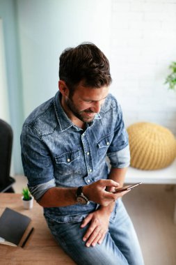 Ofisteki işadamı telefonu kullanıyor. Genç adam bir mesaj yazıyor.