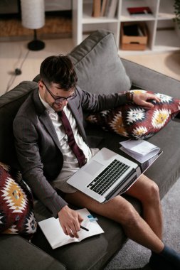 Evde pantolonsuz çalışan bir iş adamı. Genç adam video görüşmesi sırasında bilgisayarı kullanıyor..